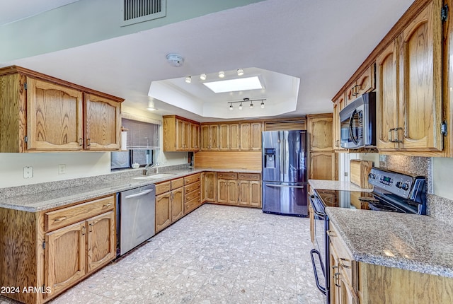 kitchen featuring a raised ceiling, stainless steel appliances, stone counters, a skylight, and sink