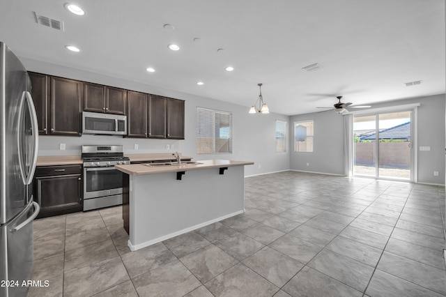 kitchen featuring a kitchen island with sink, ceiling fan with notable chandelier, hanging light fixtures, sink, and appliances with stainless steel finishes