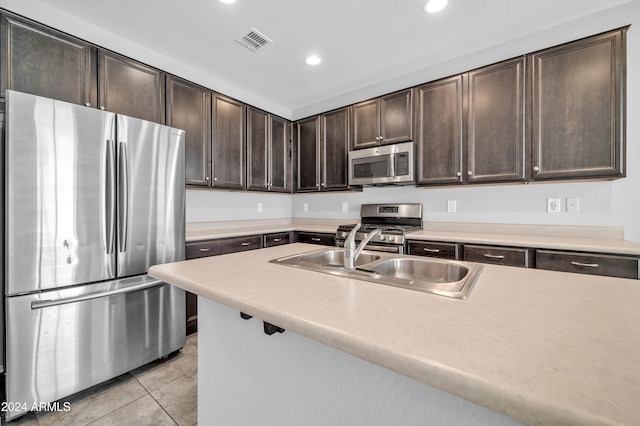 kitchen with light tile patterned flooring, dark brown cabinets, stainless steel appliances, and sink