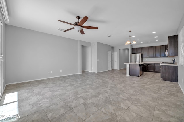 kitchen with pendant lighting, ceiling fan with notable chandelier, a kitchen island, dark brown cabinetry, and stainless steel refrigerator