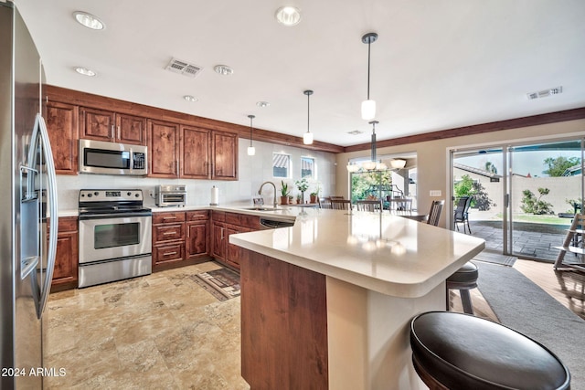 kitchen with kitchen peninsula, crown molding, pendant lighting, a kitchen bar, and appliances with stainless steel finishes