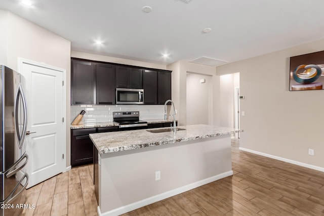 kitchen with stainless steel appliances, sink, a center island with sink, and light wood-type flooring