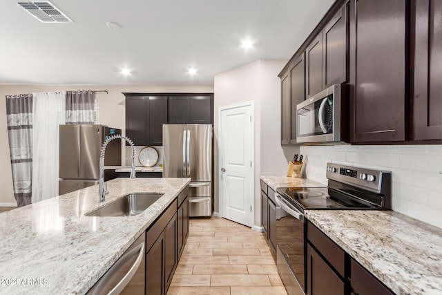 kitchen featuring sink, appliances with stainless steel finishes, dark brown cabinets, tasteful backsplash, and light stone countertops