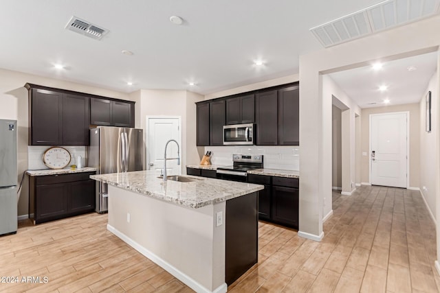 kitchen with sink, light hardwood / wood-style flooring, appliances with stainless steel finishes, a kitchen island with sink, and decorative backsplash