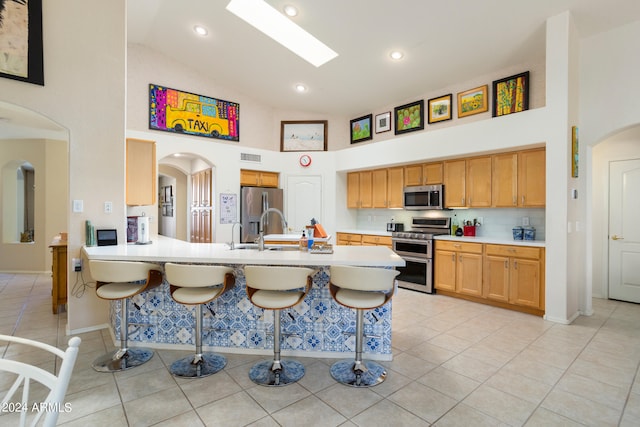 kitchen with high vaulted ceiling, appliances with stainless steel finishes, light tile floors, and a breakfast bar area