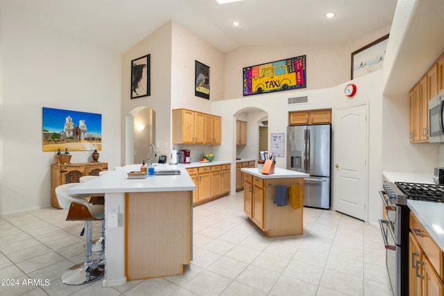 kitchen with high vaulted ceiling, a breakfast bar, appliances with stainless steel finishes, sink, and an island with sink