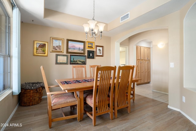 dining room with a chandelier, light wood-type flooring, and a tray ceiling