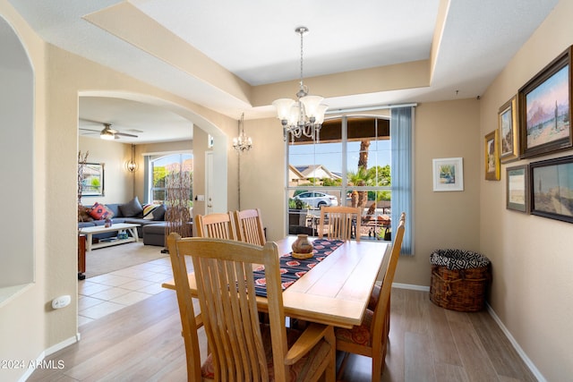 dining room with ceiling fan with notable chandelier, a raised ceiling, and light hardwood / wood-style floors