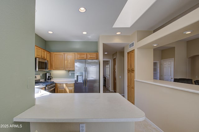 kitchen with a skylight, stainless steel appliances, kitchen peninsula, and light brown cabinets