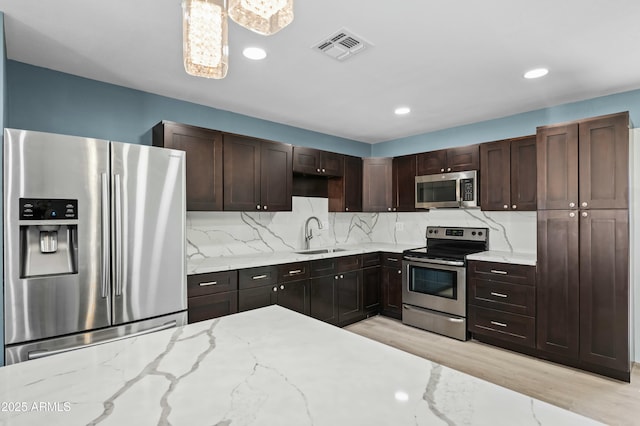 kitchen with sink, tasteful backsplash, light stone counters, light hardwood / wood-style floors, and appliances with stainless steel finishes