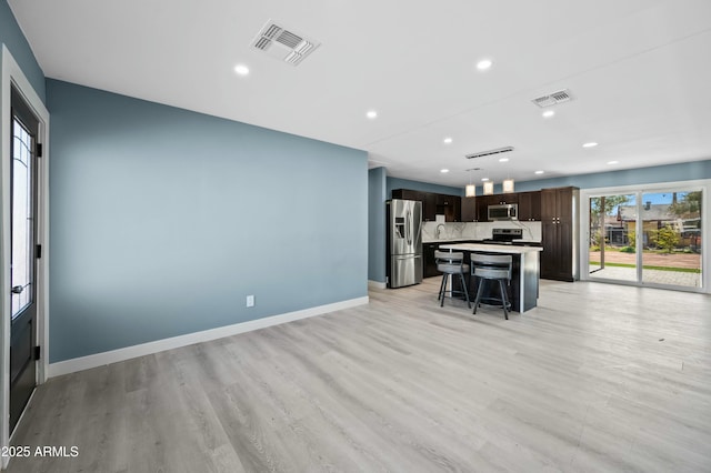 kitchen featuring a center island, stainless steel appliances, backsplash, light hardwood / wood-style floors, and a breakfast bar area