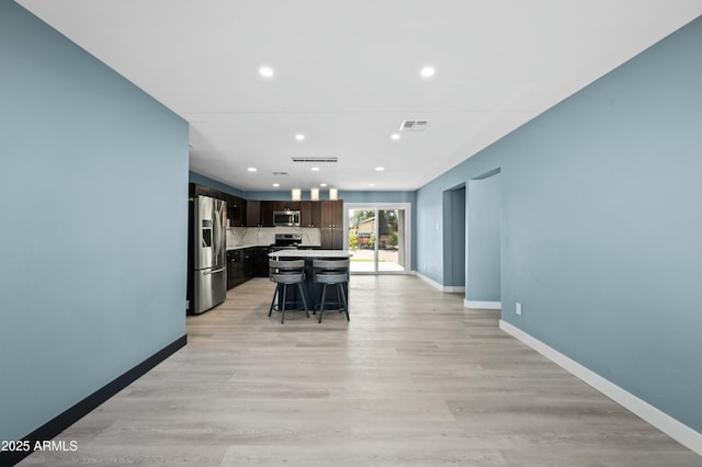 kitchen with a center island, stainless steel appliances, a breakfast bar, dark brown cabinets, and light wood-type flooring