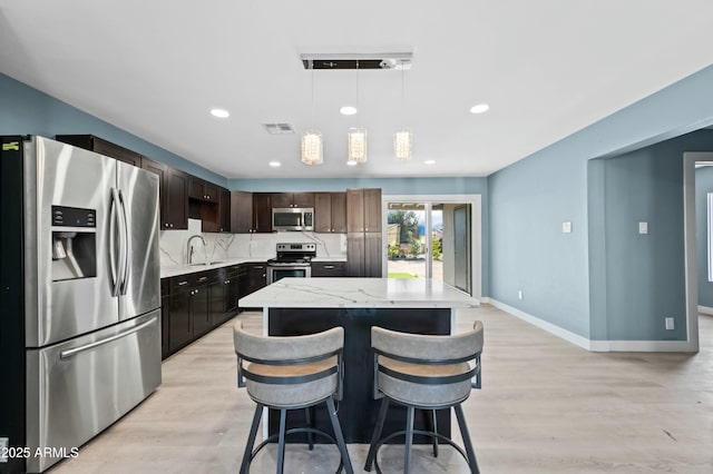 kitchen featuring hanging light fixtures, stainless steel appliances, decorative backsplash, a breakfast bar, and a kitchen island