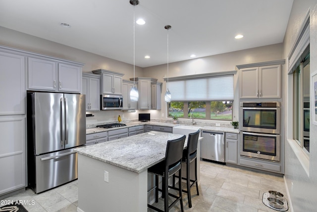 kitchen with appliances with stainless steel finishes, a center island, hanging light fixtures, light stone counters, and a breakfast bar area