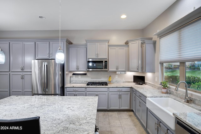 kitchen with stainless steel appliances, gray cabinetry, light stone countertops, pendant lighting, and sink