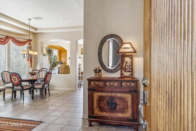 interior space with light tile patterned floors, arched walkways, a chandelier, visible vents, and baseboards