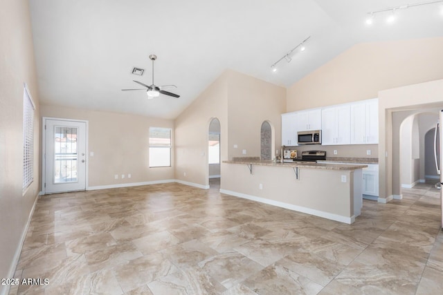 kitchen featuring a kitchen bar, appliances with stainless steel finishes, high vaulted ceiling, white cabinets, and light stone counters