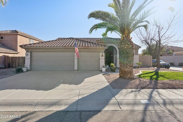 mediterranean / spanish-style house featuring a tile roof, stucco siding, fence, a garage, and driveway