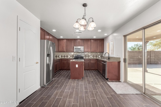 kitchen with hanging light fixtures, an inviting chandelier, backsplash, a kitchen island, and appliances with stainless steel finishes