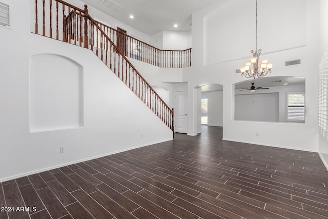 unfurnished living room with plenty of natural light, ceiling fan with notable chandelier, and a high ceiling