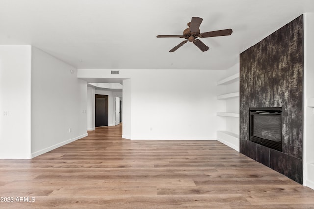 unfurnished living room featuring ceiling fan, light hardwood / wood-style floors, and a large fireplace