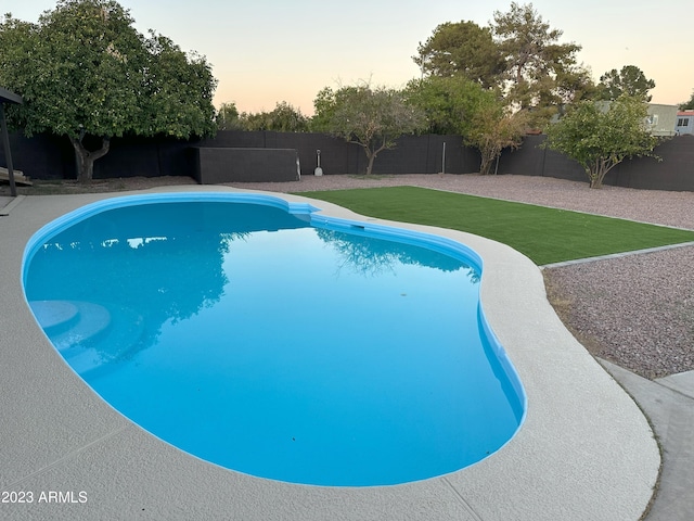 pool at dusk featuring a yard