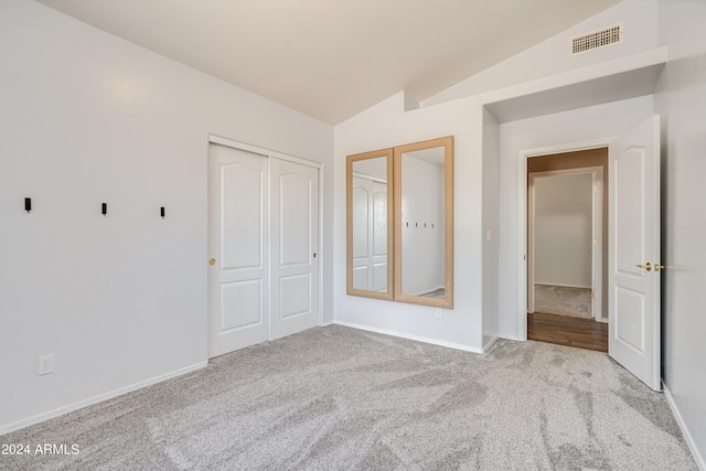 unfurnished bedroom with light carpet, a closet, and lofted ceiling