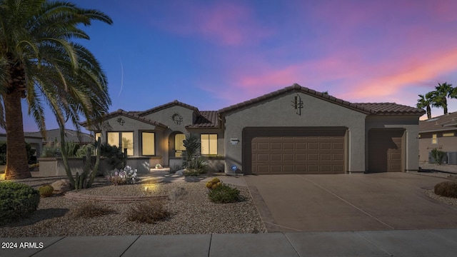 mediterranean / spanish home featuring a garage, a tile roof, driveway, and stucco siding