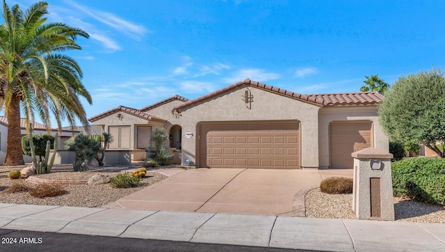 mediterranean / spanish house with driveway, an attached garage, a tiled roof, and stucco siding