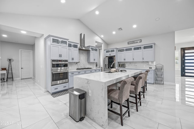 8017 S 143rd Ave, Goodyear, AZ 85338 - kitchen featuring stainless steel double oven, wall chimney exhaust hood, lofted ceiling, light marble finish flooring, and a spacious island