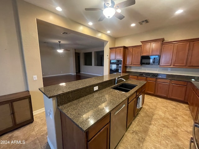 kitchen with ceiling fan, sink, dark stone counters, a center island with sink, and black appliances