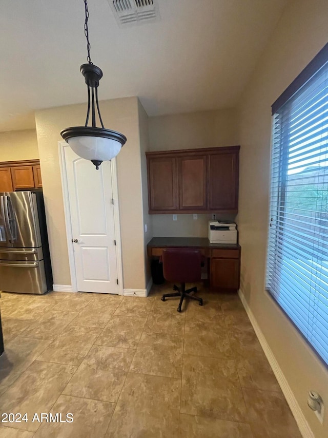 kitchen featuring stainless steel fridge, built in desk, and hanging light fixtures