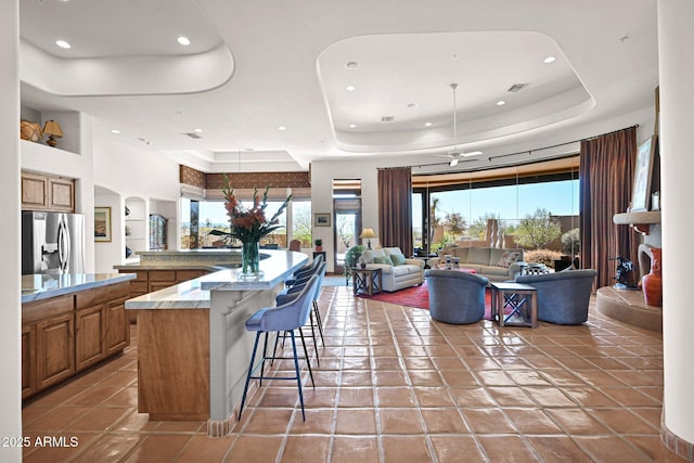 kitchen featuring stainless steel refrigerator with ice dispenser, a kitchen breakfast bar, open floor plan, light tile patterned flooring, and a raised ceiling