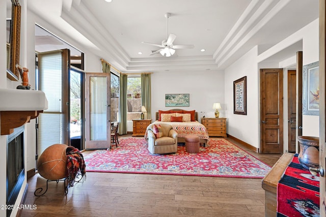 bedroom featuring baseboards, a tray ceiling, recessed lighting, a fireplace, and wood finished floors