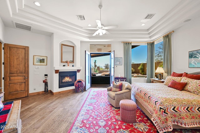 bedroom with a raised ceiling, wood finished floors, visible vents, and a lit fireplace