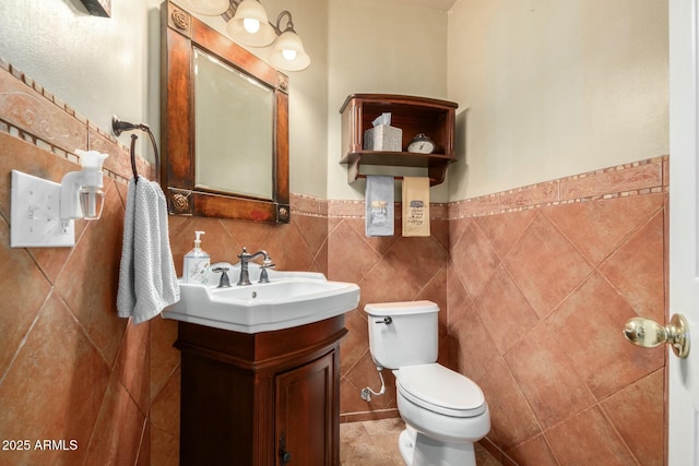 bathroom with toilet, tile walls, wainscoting, and vanity