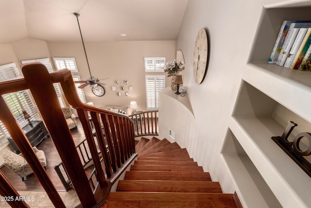 staircase with lofted ceiling, wood finished floors, visible vents, and ceiling fan