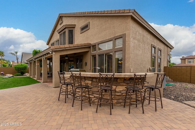 back of house featuring a patio, fence, ceiling fan, stucco siding, and outdoor dry bar