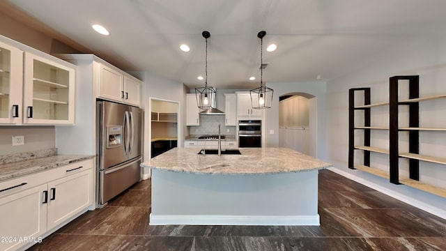 kitchen with appliances with stainless steel finishes, hanging light fixtures, light stone counters, a kitchen island with sink, and white cabinets