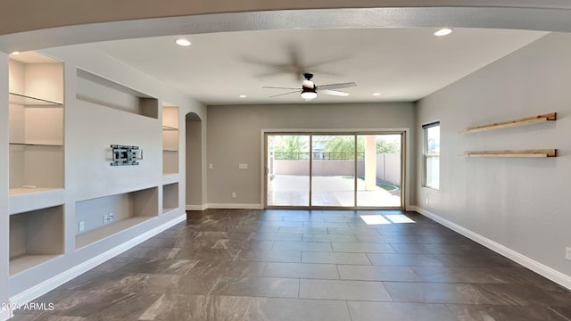 unfurnished living room featuring ceiling fan, built in shelves, and dark tile floors