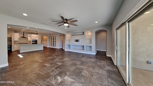 unfurnished living room featuring dark tile flooring, ceiling fan, and built in shelves