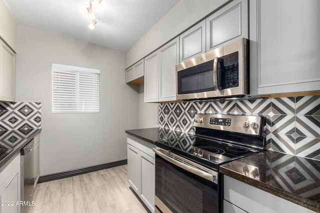 kitchen featuring decorative backsplash, appliances with stainless steel finishes, dark stone countertops, and light hardwood / wood-style flooring