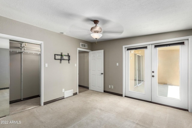 unfurnished bedroom with a textured ceiling, light carpet, french doors, a closet, and ceiling fan