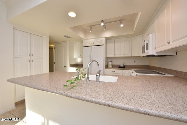 kitchen with white appliances, white cabinets, a raised ceiling, sink, and light tile patterned floors