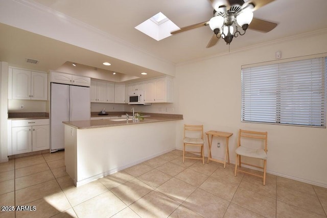 kitchen with white cabinets, kitchen peninsula, white appliances, light tile patterned floors, and ornamental molding