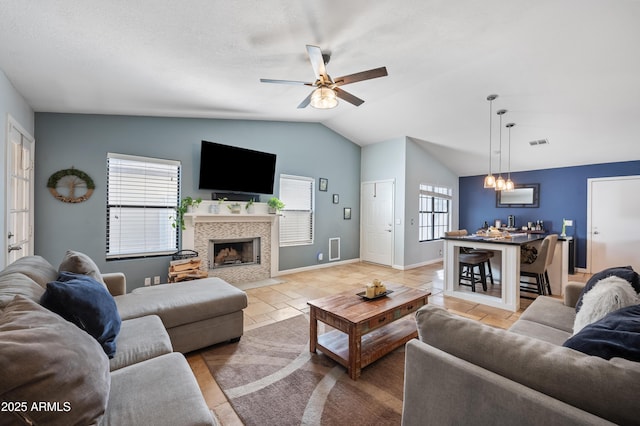 living room with a healthy amount of sunlight, ceiling fan, lofted ceiling, and a tiled fireplace