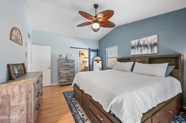 bedroom with lofted ceiling, light hardwood / wood-style flooring, ceiling fan, a barn door, and connected bathroom