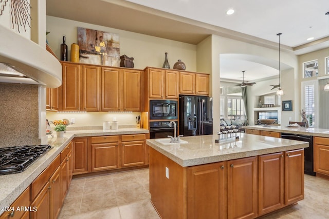 kitchen with a sink, exhaust hood, brown cabinets, black appliances, and decorative light fixtures