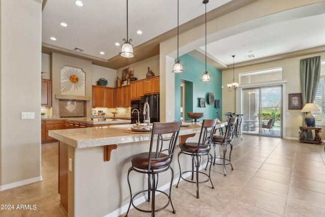 kitchen featuring brown cabinetry, a breakfast bar area, backsplash, pendant lighting, and a sink