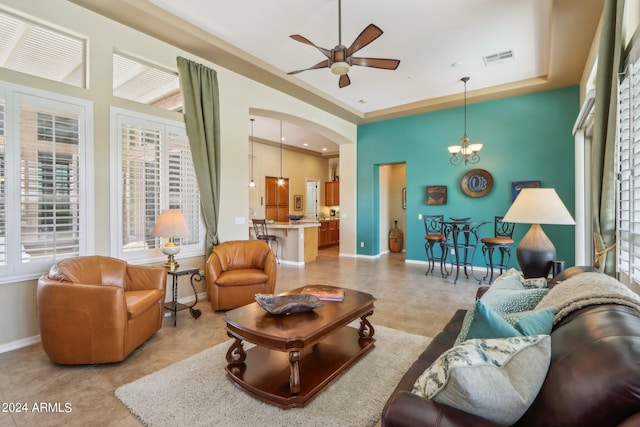 living room with baseboards, visible vents, a raised ceiling, and ceiling fan with notable chandelier